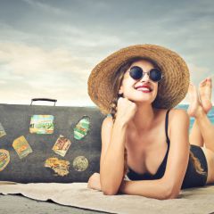 Frau mit Sonnenhut und Reisekoffer am Ostseestrand